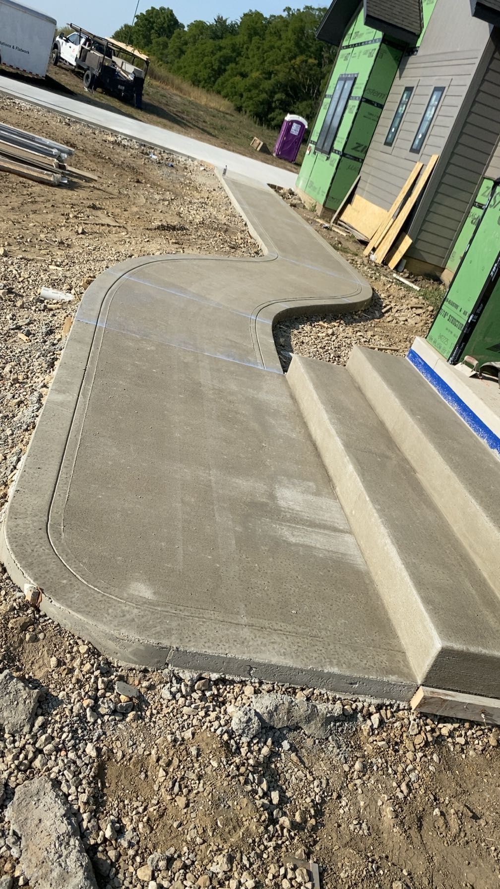 Newly poured concrete sidewalk with steps and curved path, near construction site.