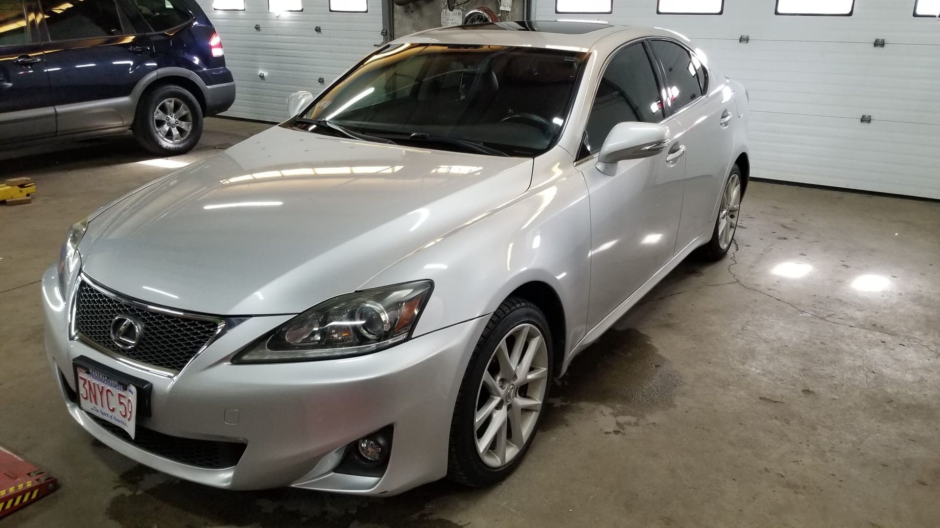 A silver Lexus is parked in a garage next to a blue SUV.