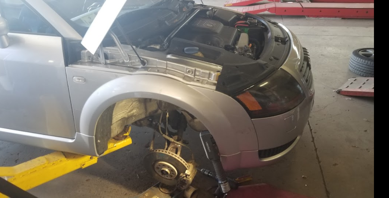 A silver car with the hood up is on a lift in a garage.