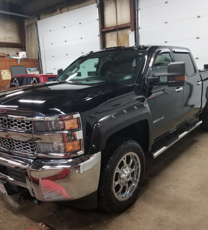 A black truck is parked in a garage next to a garage door.