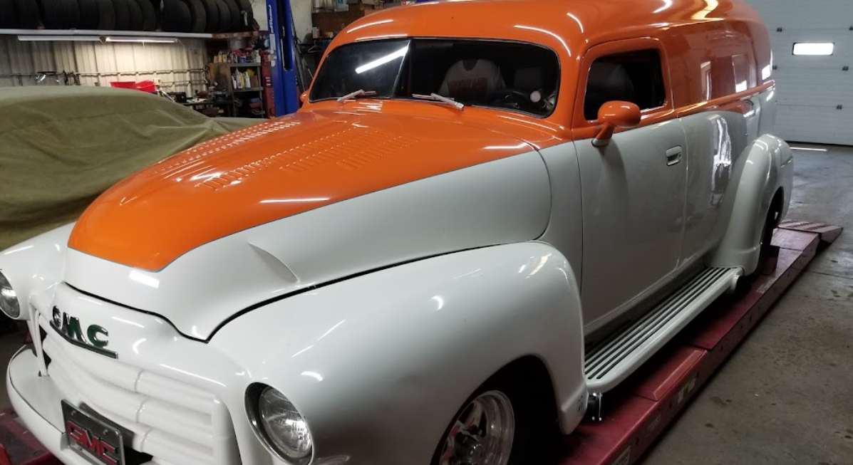 A white and orange car is parked on a lift in a garage.