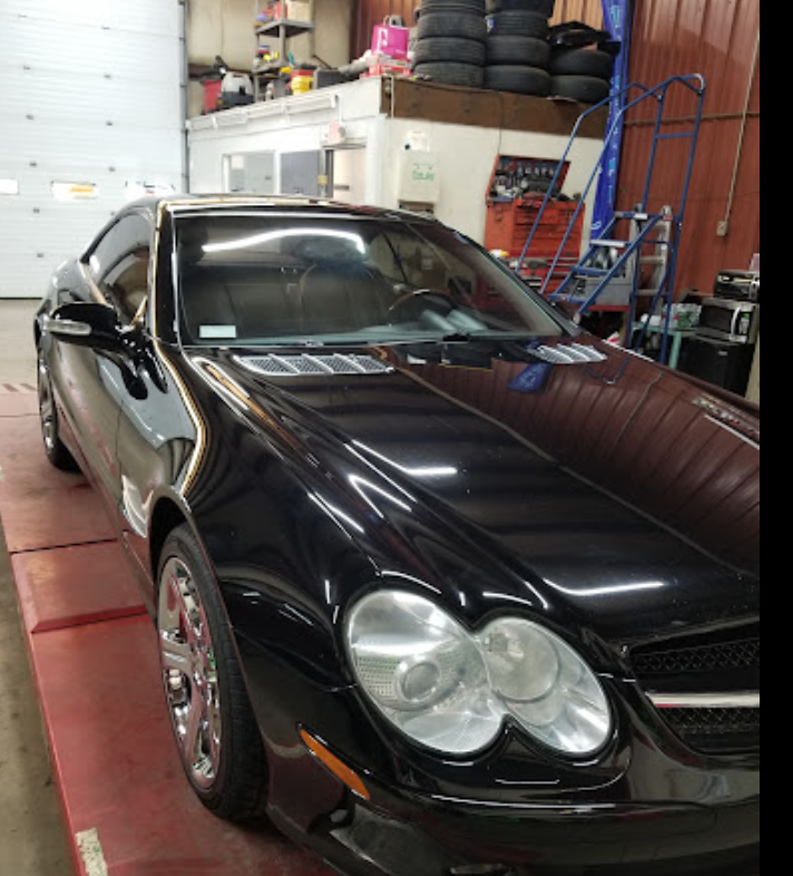 A black car is parked in a garage next to a bunch of tires