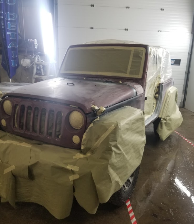 A jeep is covered in plastic wrap in a garage