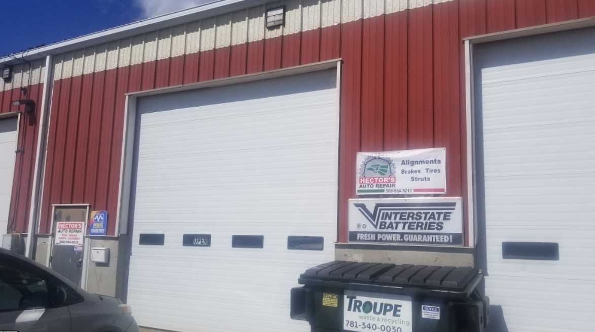 A car is parked in front of a red building with white garage doors.