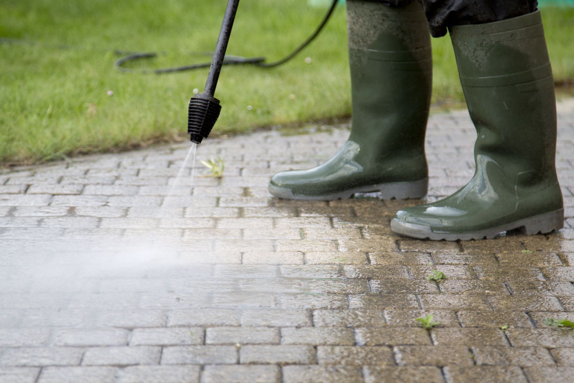 Person in green boots pressure washing a brick path outdoors