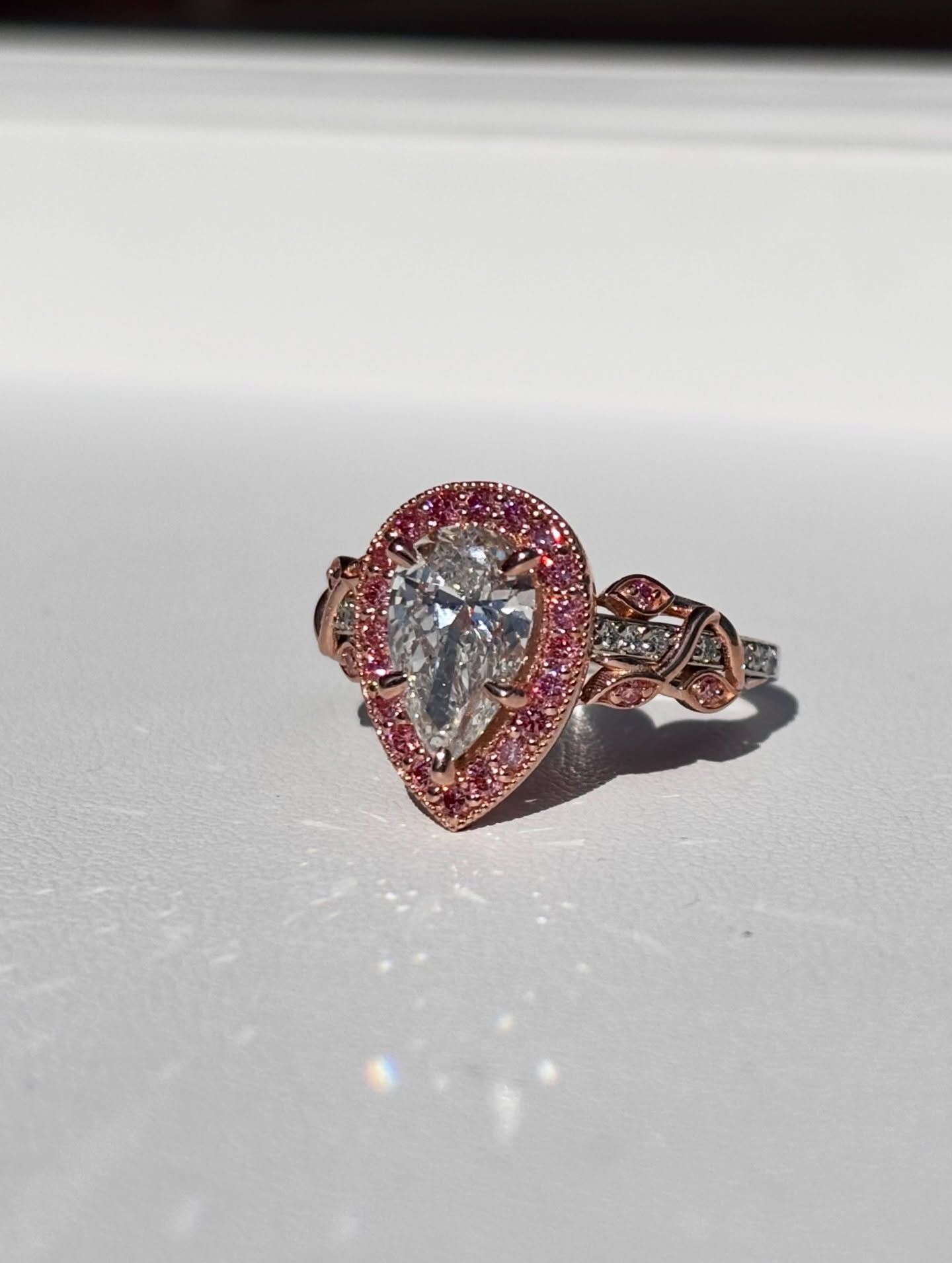 Teardrop-shaped pink gemstone ring with a silver band on a white surface