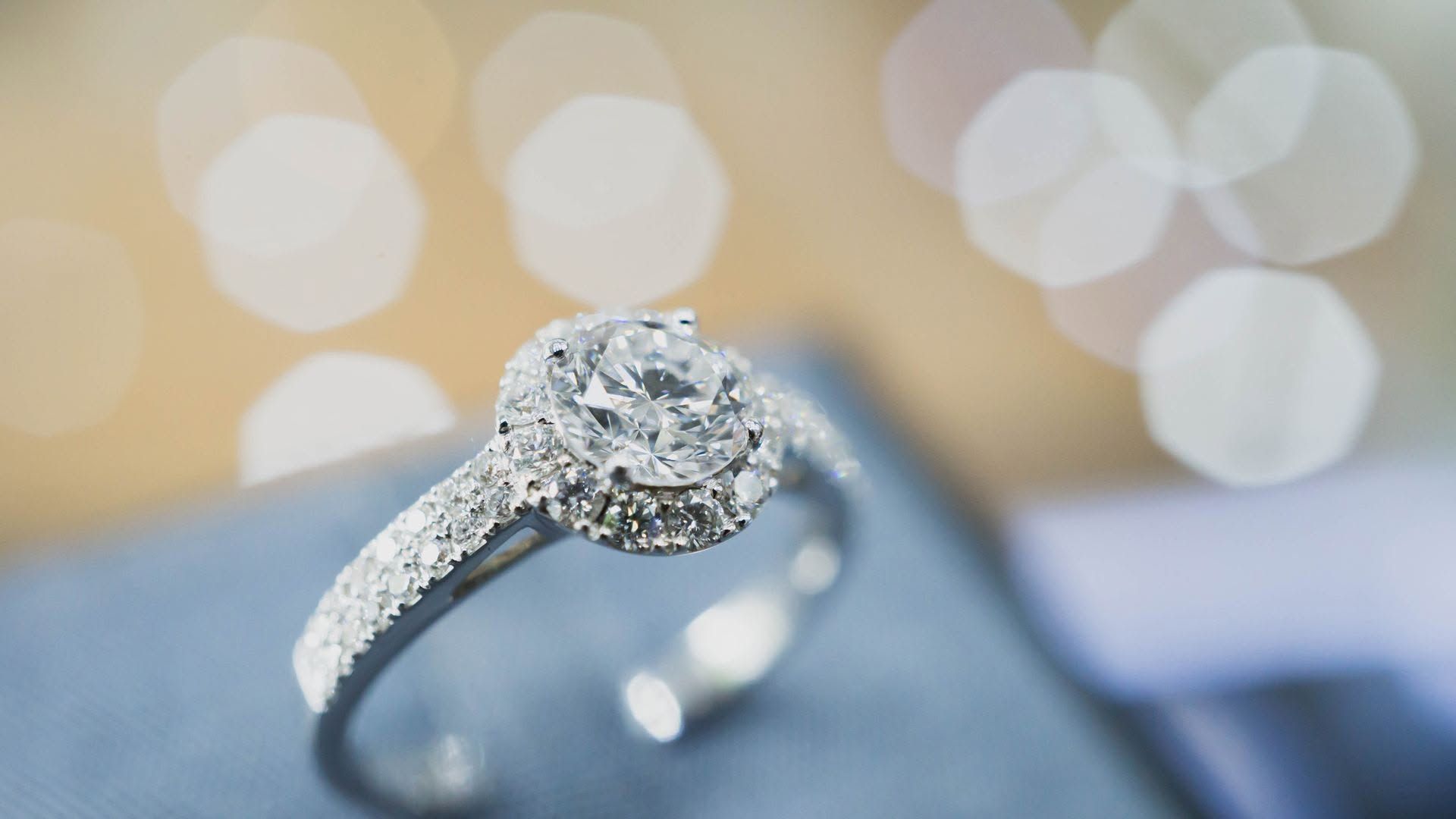 Diamond engagement ring on a blue surface with blurred bokeh lights in the background