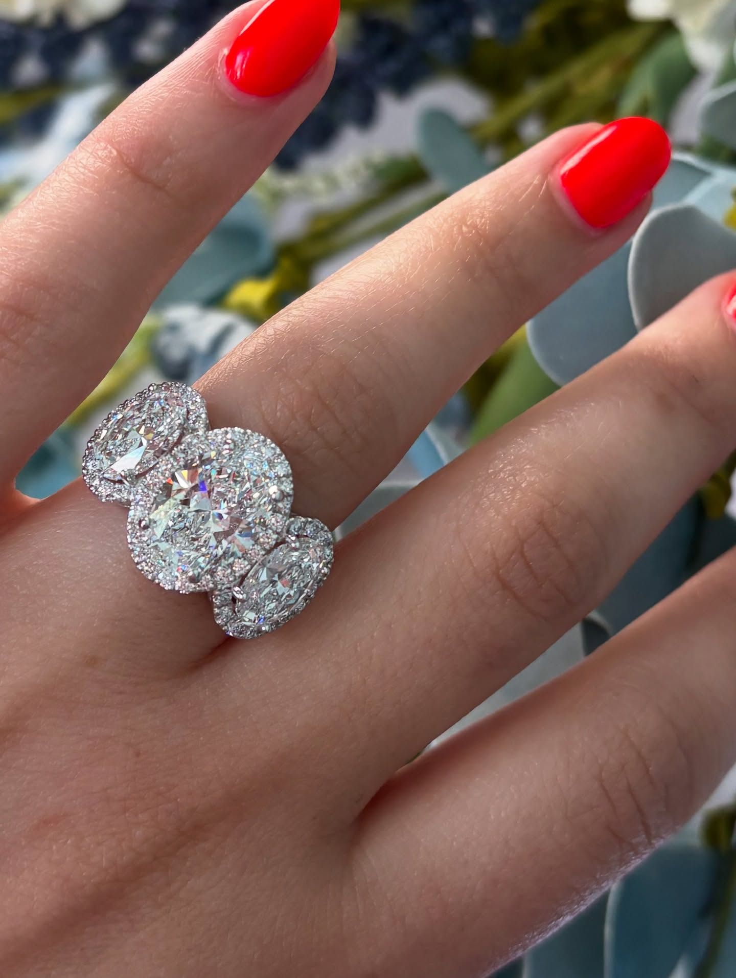 Hand with bright red nails wearing a sparkling multi-stone ring outdoors