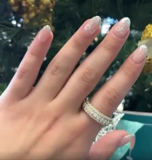 Hand with glittery nails and a diamond ring held up outdoors against a blurred green background