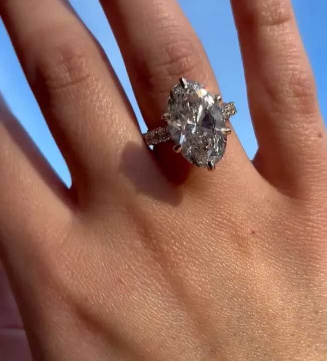 Close-up of a hand wearing a large oval diamond ring against a blue sky.