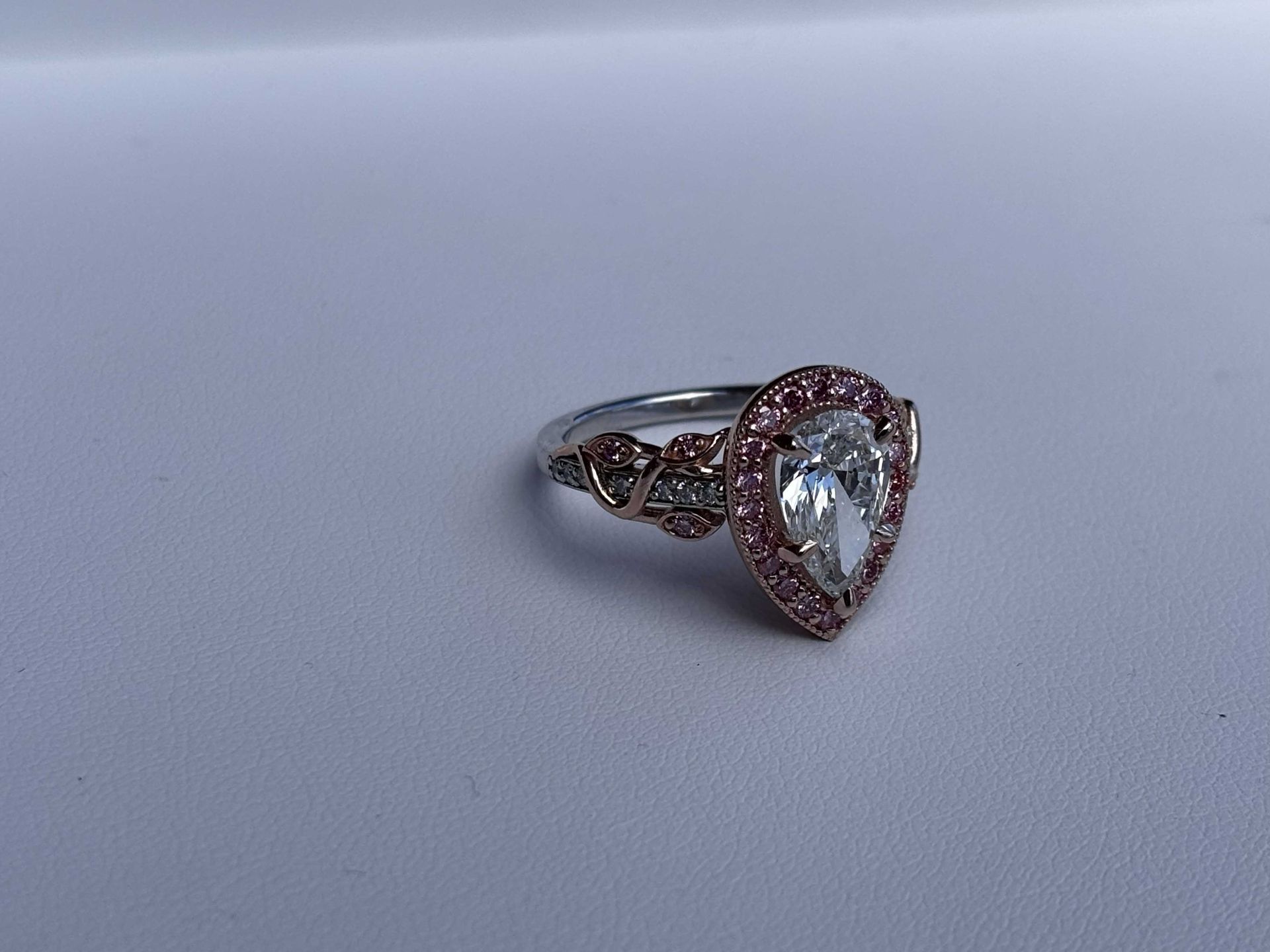 Rose gold pear-shaped ring with a clear gemstone and pave accents on a light gray surface