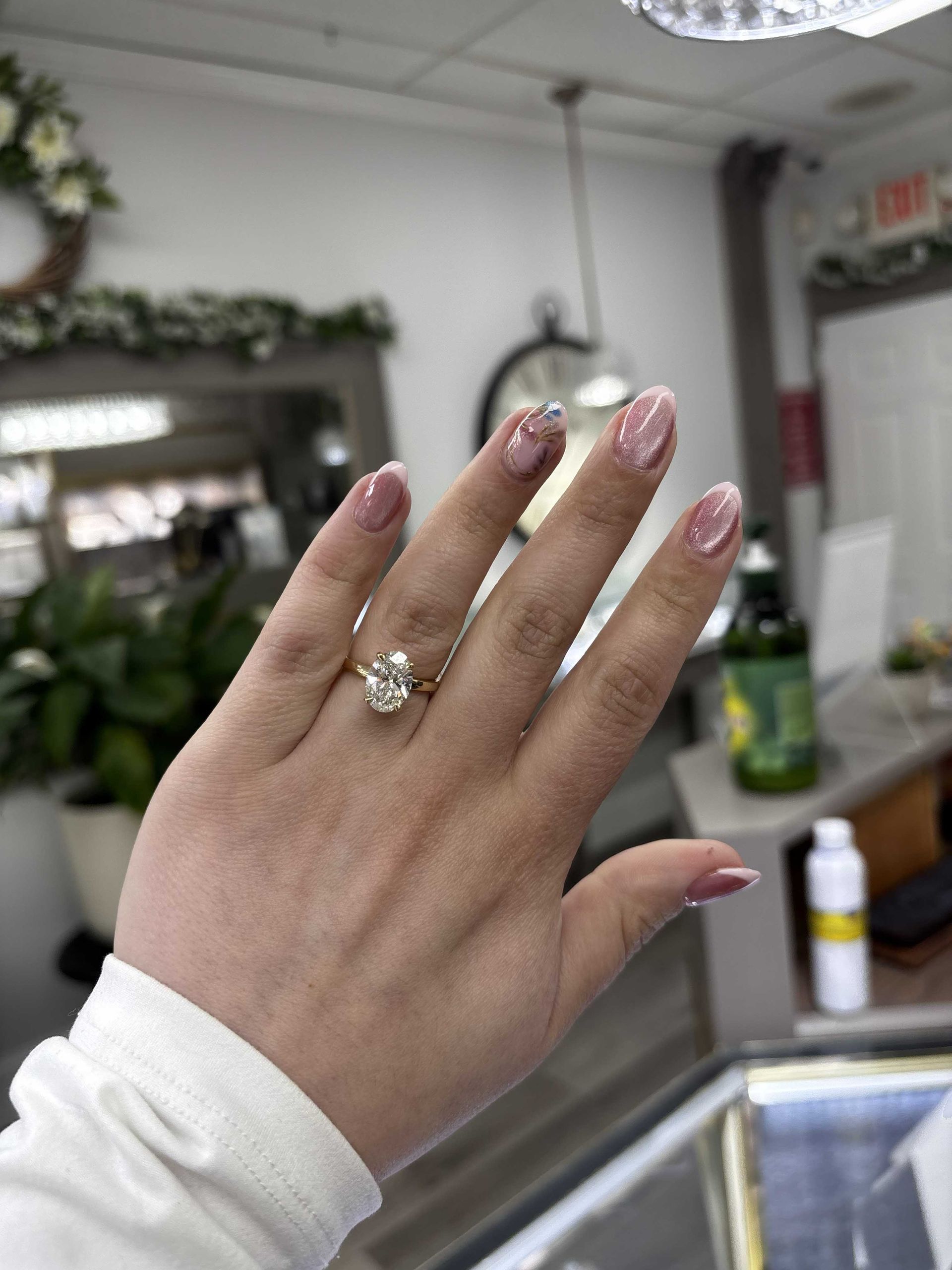 Hand with glittery pink nails and diamond ring held up in a salon mirror.