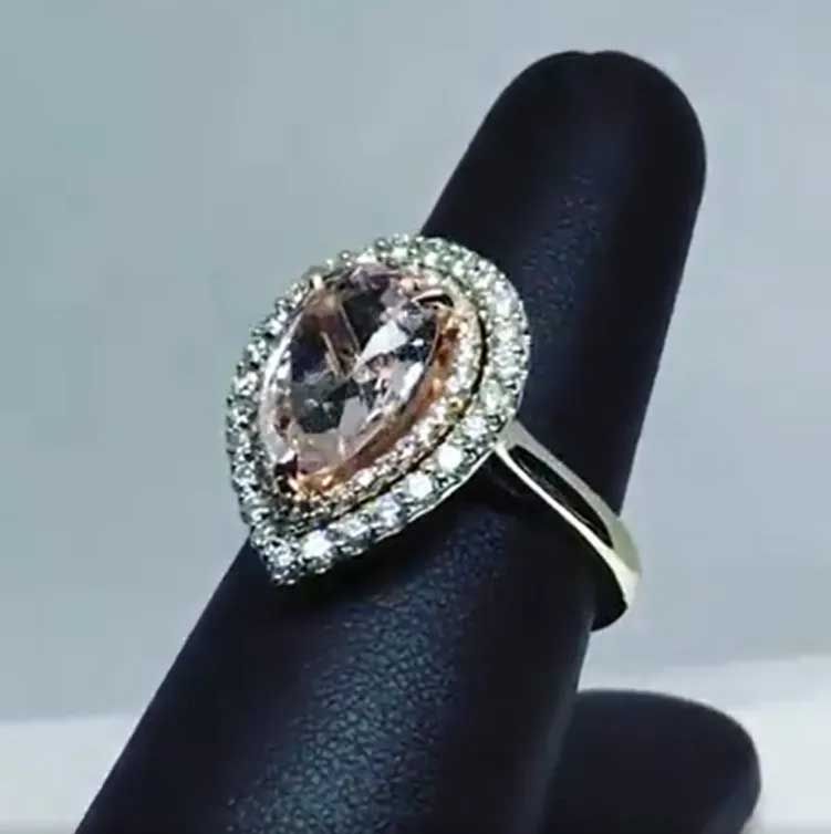 Pear-shaped rose-gold gemstone ring with a double halo of clear stones on a black display stand
