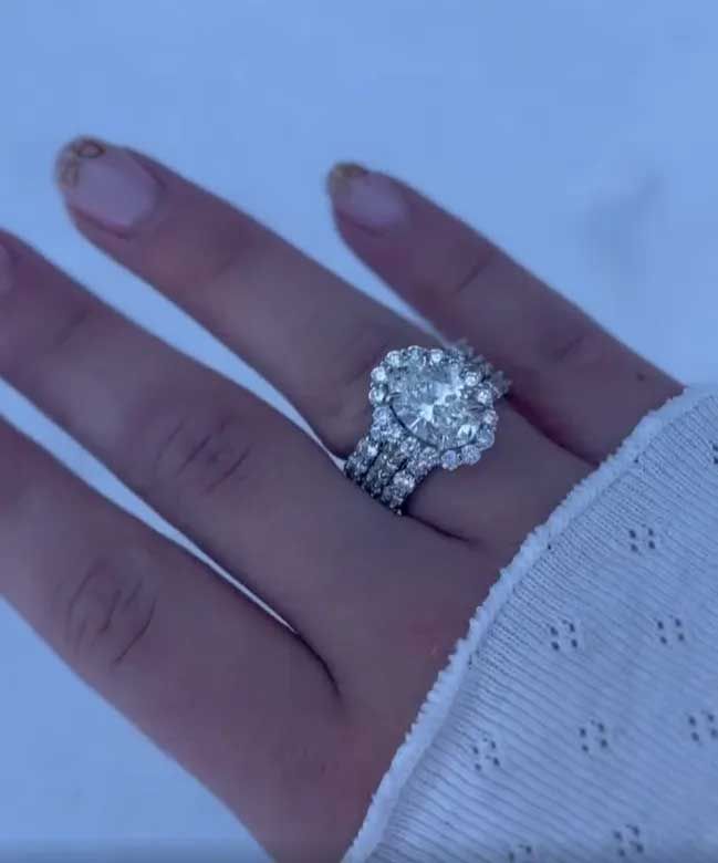 Hand wearing a large sparkling ring against a light blue background