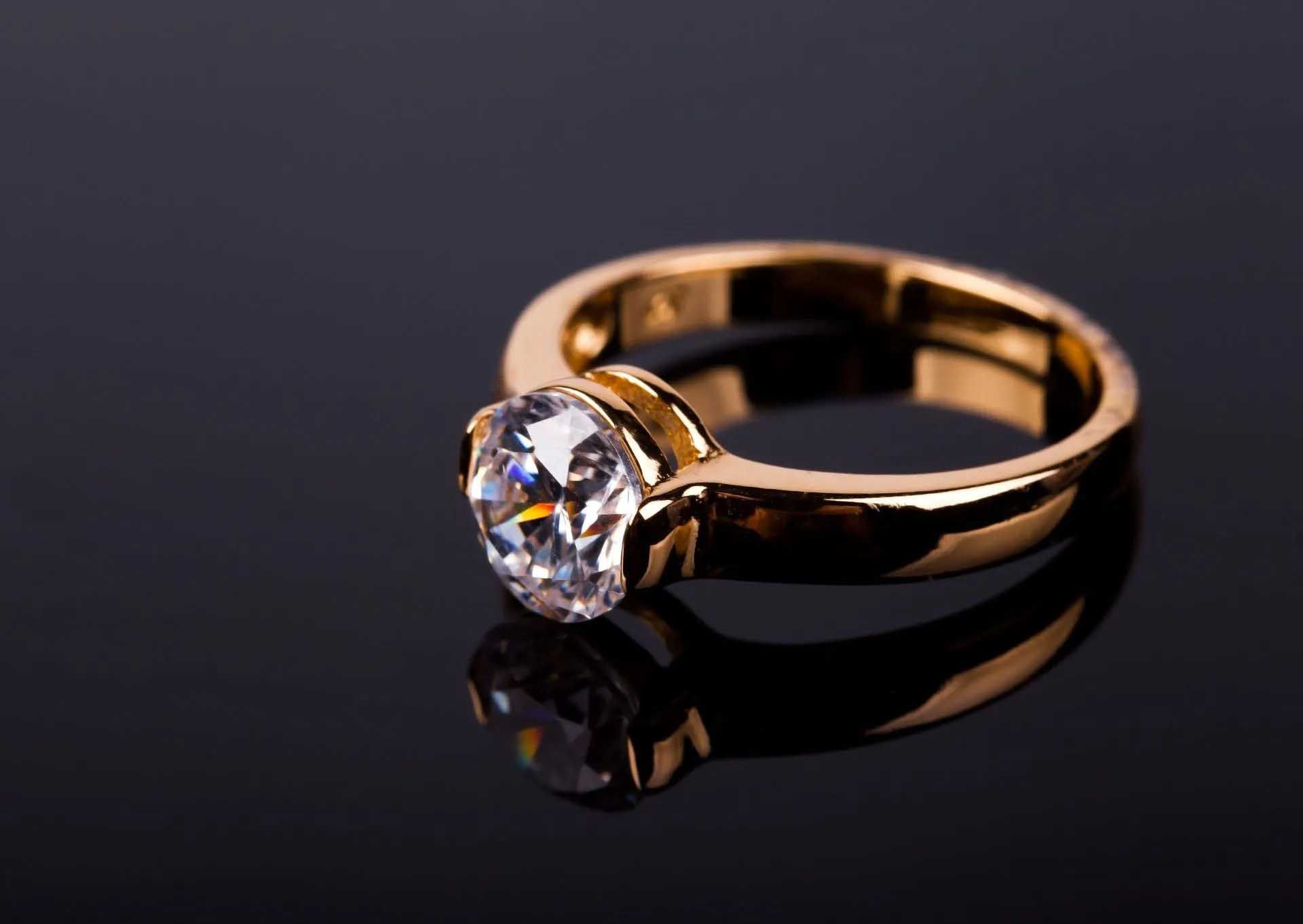 Gold ring with a clear gemstone on a dark reflective surface