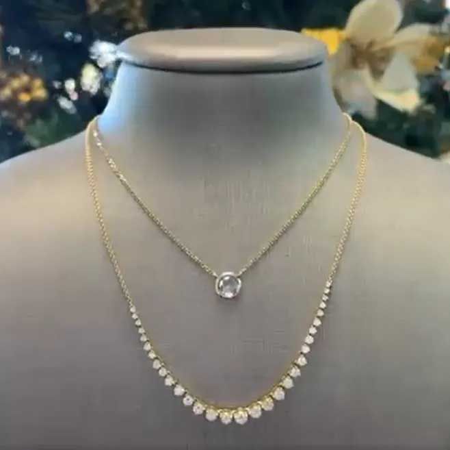 Two layered gold necklaces displayed on a gray bust, one with a round pendant and one with teardrop stones