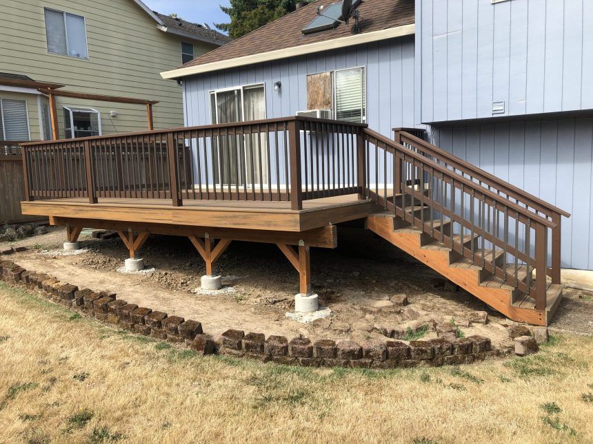 A wooden deck with stairs leading up to it is in front of a blue house.