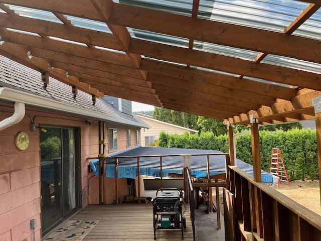 A wooden deck with a clear roof is being built on the side of a house.