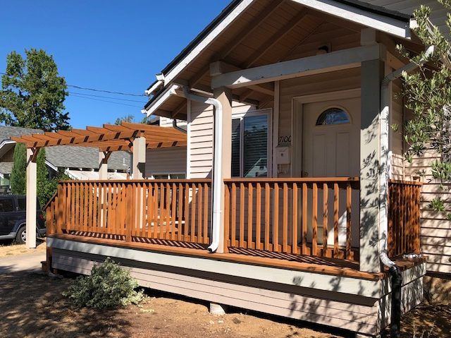 A small house with a large porch and a car parked in front of it.