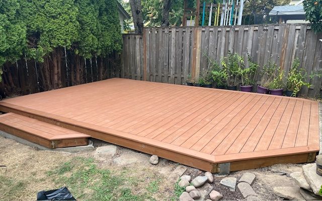 A wooden deck in a backyard next to a wooden fence.