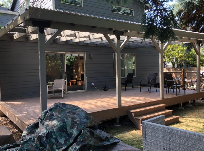 A large deck with a pergola and chairs in front of a house.
