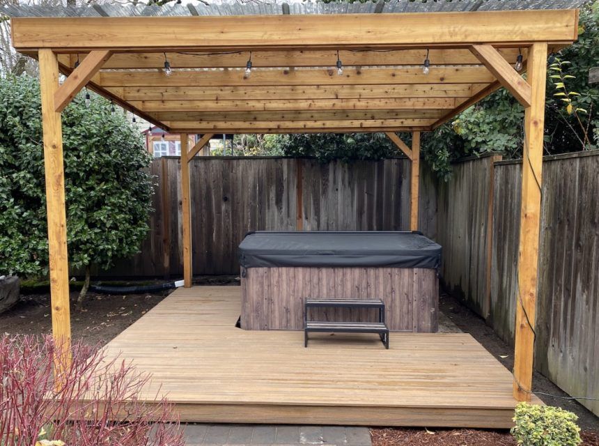 A hot tub is sitting under a wooden pergola in a backyard.