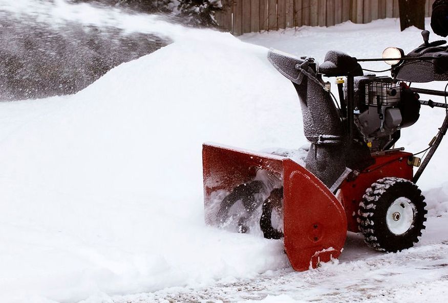 Snowblower expelling snow from a driveway; white snow, red machine, winter setting.