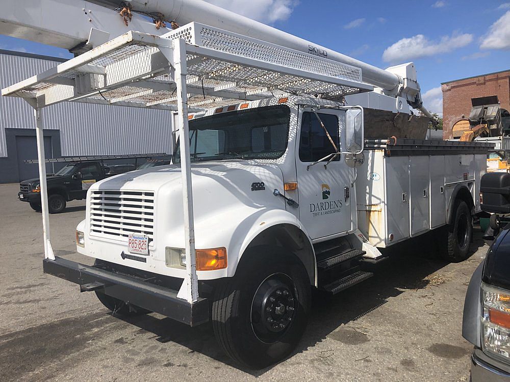 White utility truck with storage compartments and overhead rack parked outside.