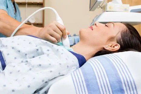 A woman is laying in a hospital bed getting an ultrasound of her neck.
