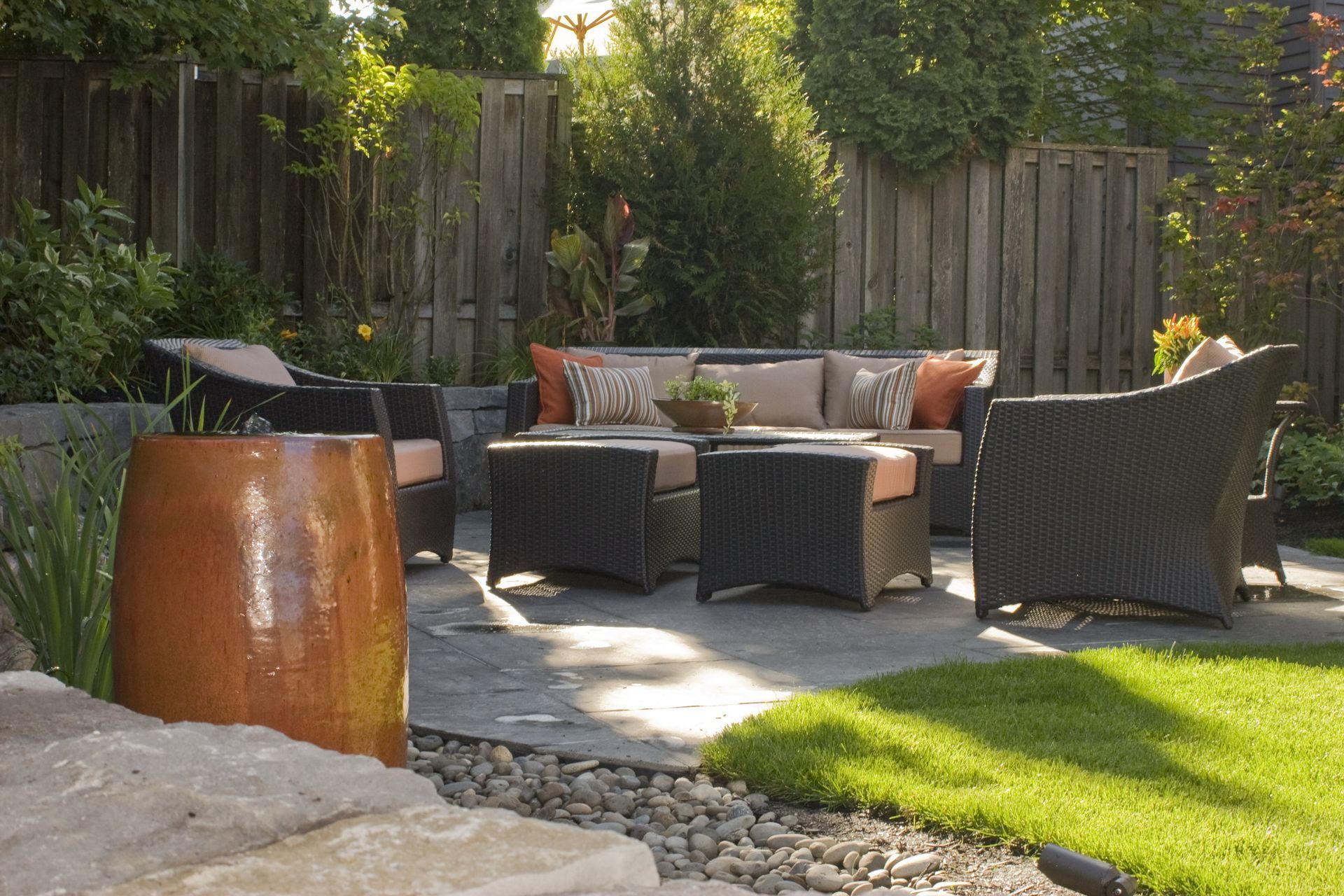 Backyard patio with wicker chairs, outdoor sofa, fire pit, and green lawn in sunlight