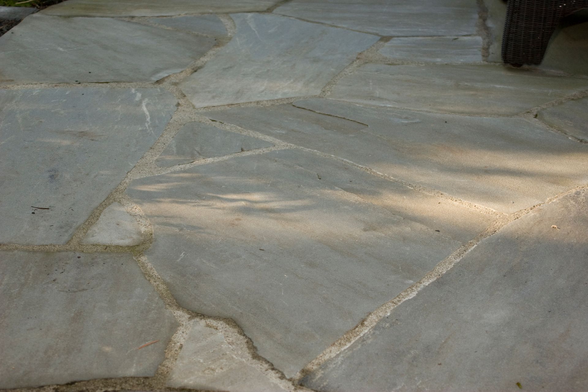 Cracked stone patio with irregular beige slabs and sunlight shadows