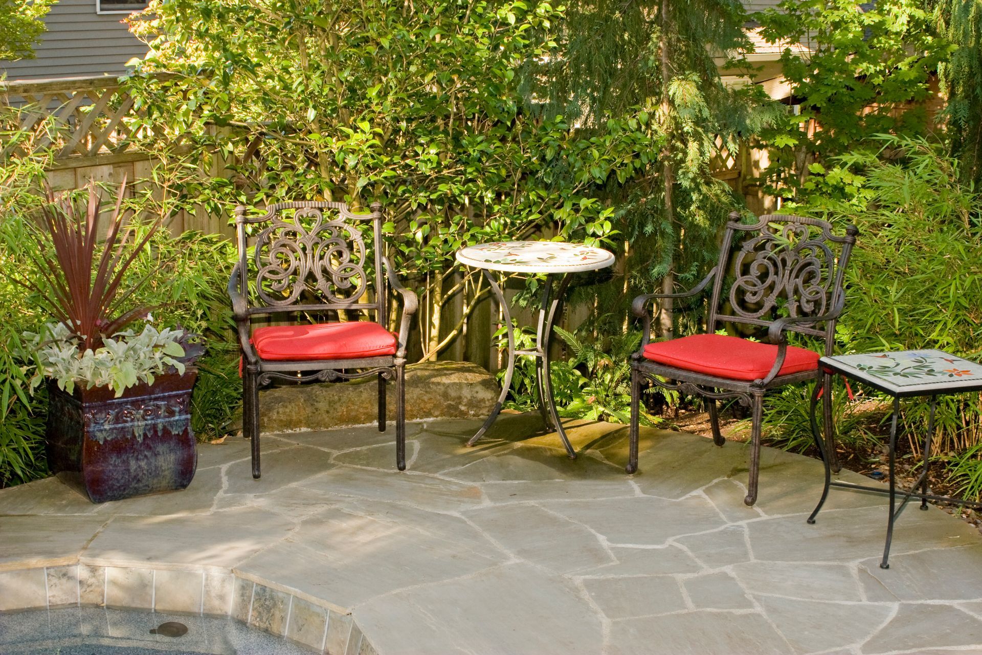 Patio with two red-cushioned chairs, a small table, and potted plants beside a garden wall