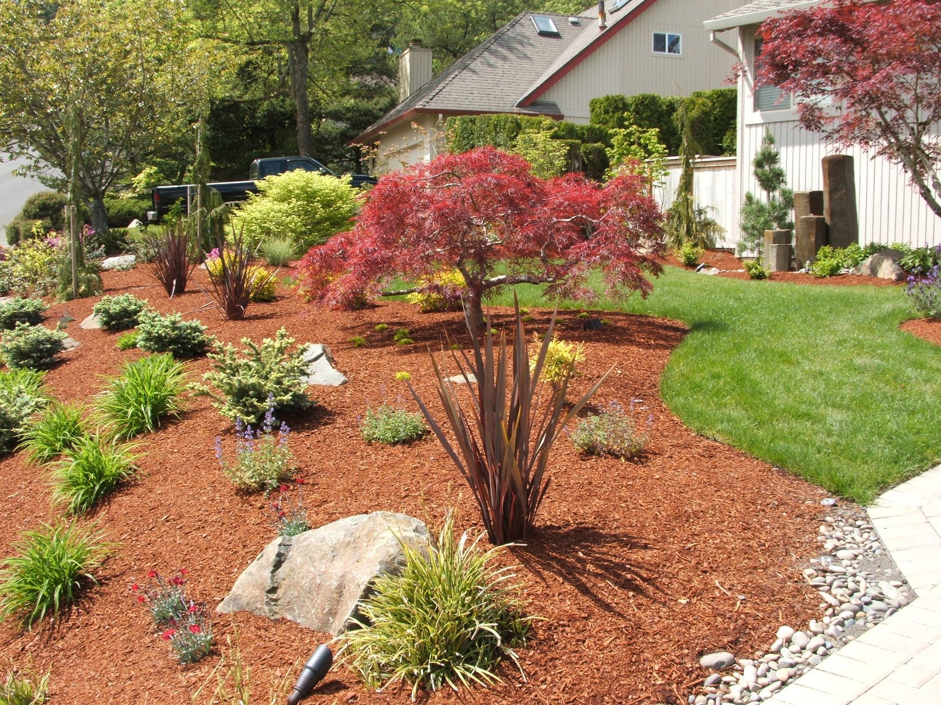 Landscaped front yard with red mulch, shrubs, a small tree, and a house in the background