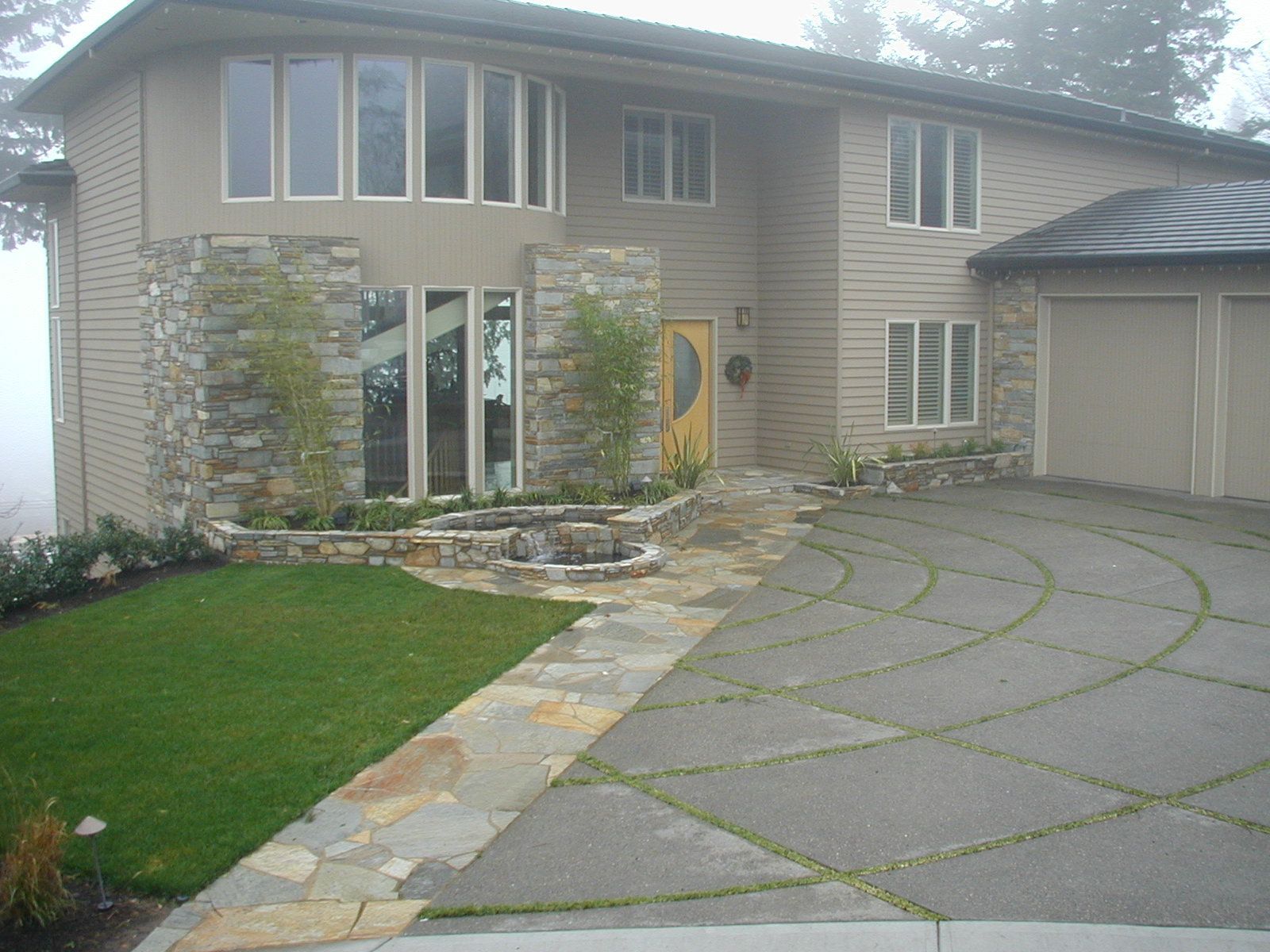 Suburban house exterior with curved stone driveway, green lawn, and large front windows