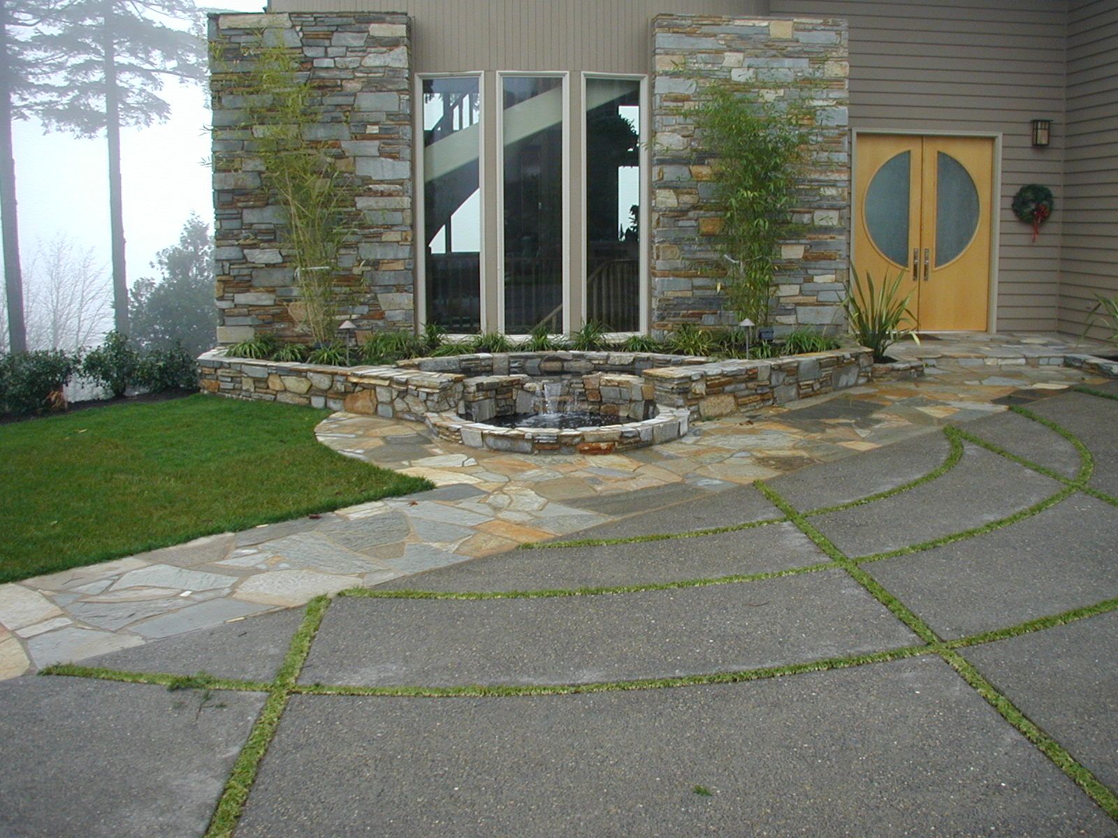 Front entrance with stone columns, glass door, curved concrete driveway, and landscaped yard.