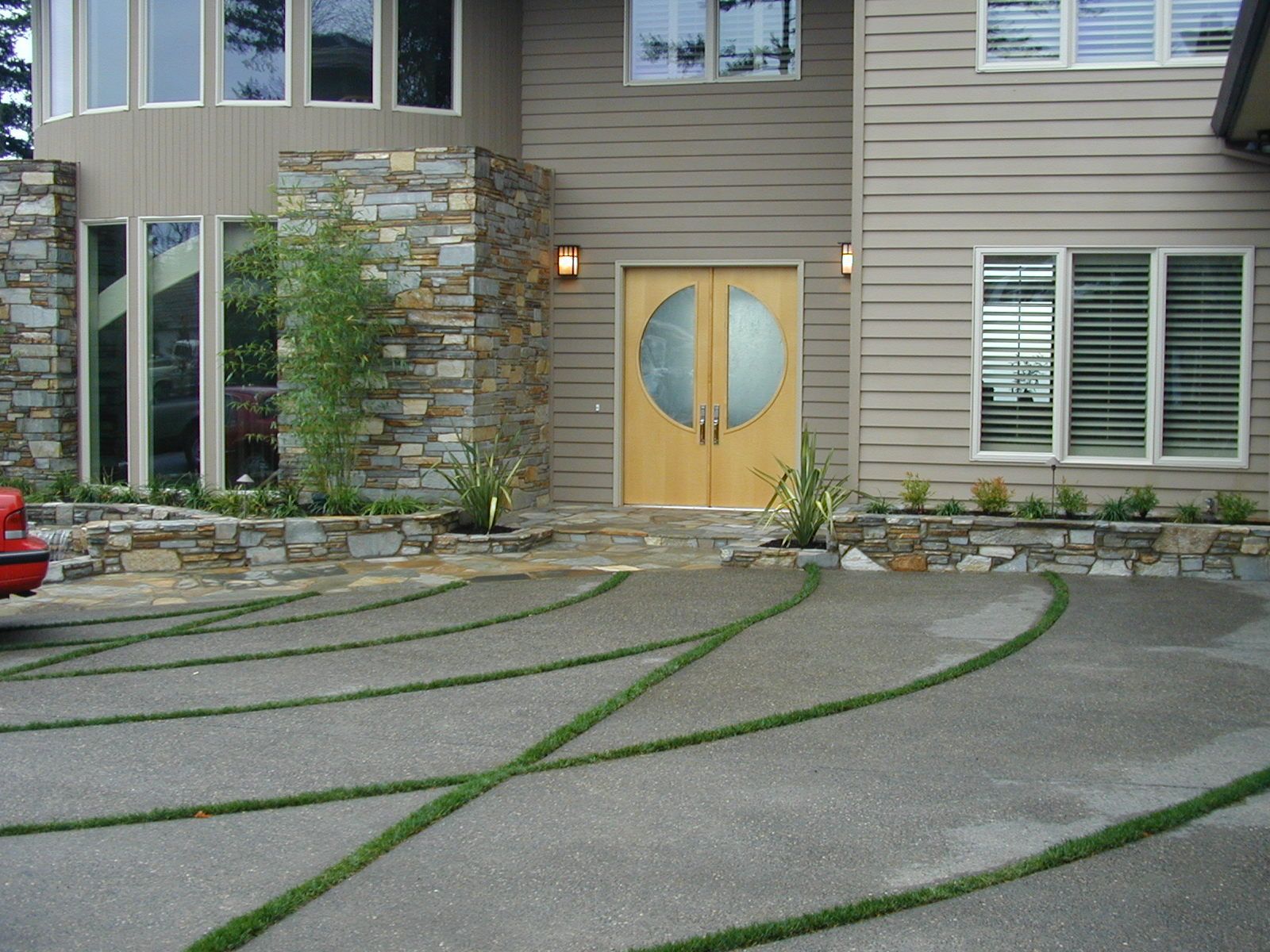 Modern house exterior with stone entrance, double doors, and curved driveway lines