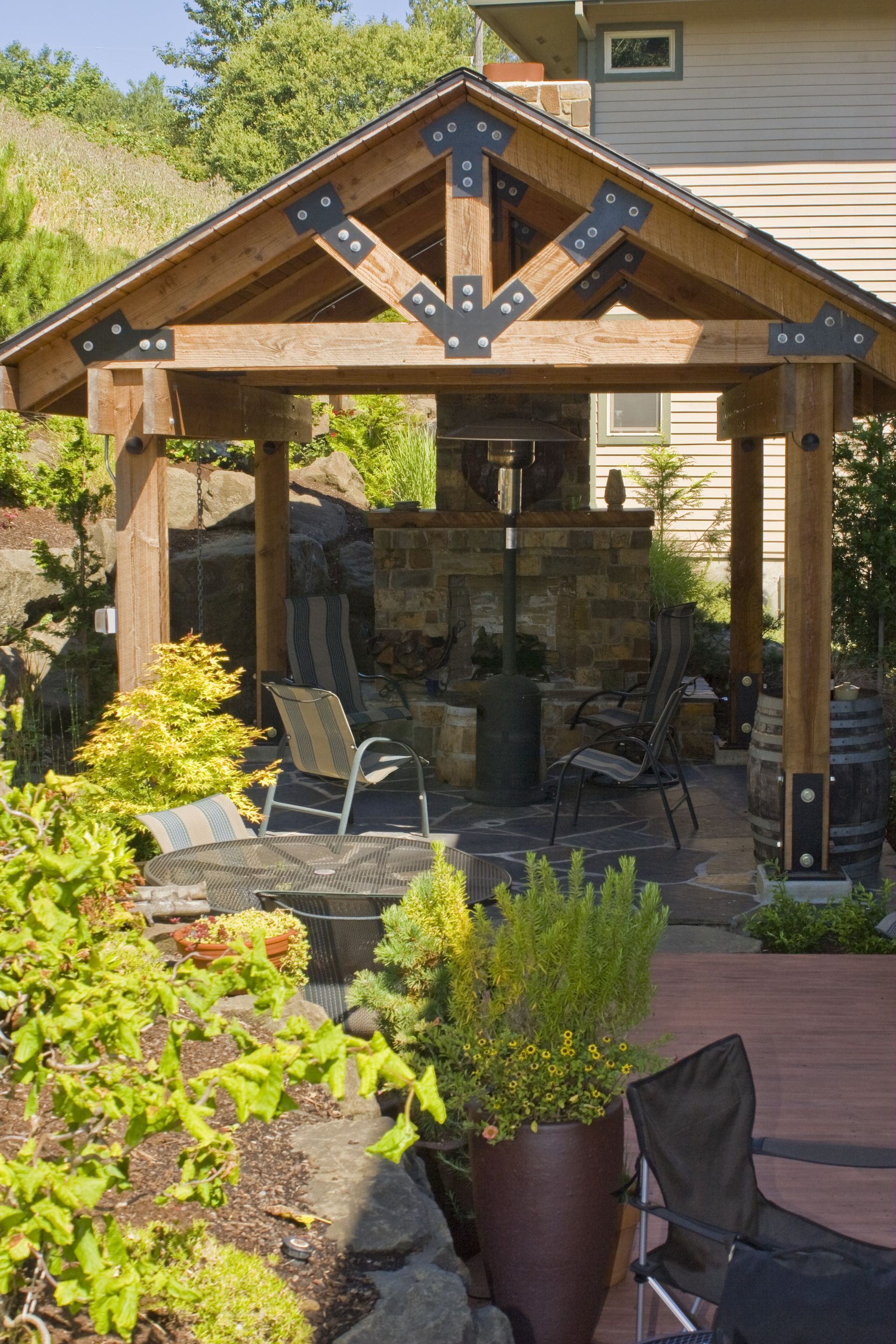 Wooden backyard gazebo with stone fireplace, string lights, and outdoor seating surrounded by plants