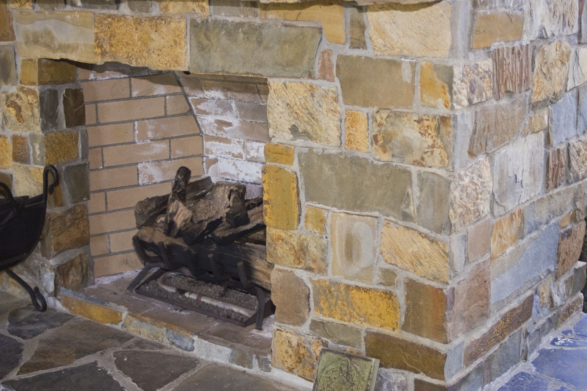 Stone fireplace with a black metal fire grate inside a brick-lined hearth