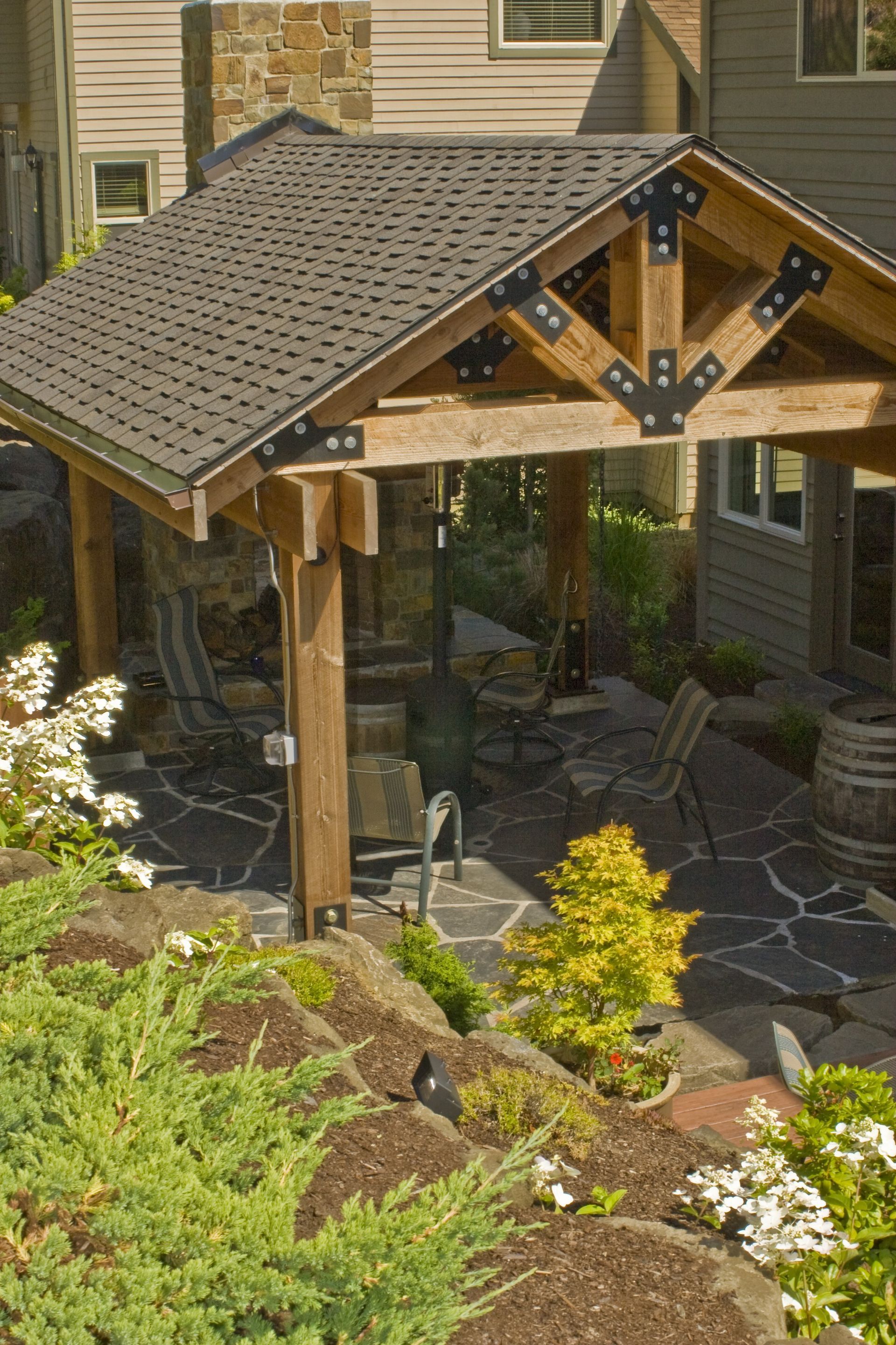 Covered patio with a wooden pergola, stone floor, and outdoor seating beside a house