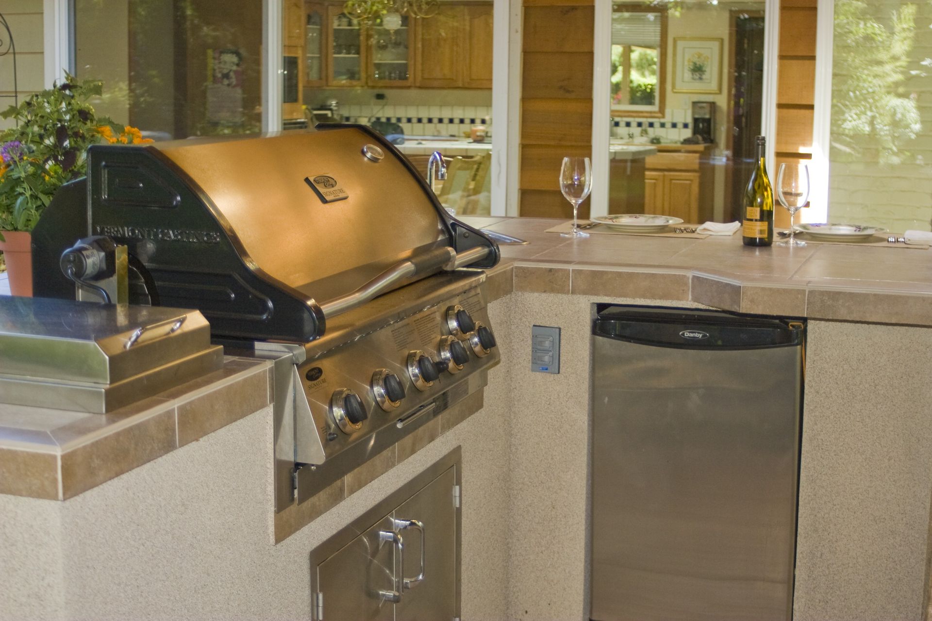 Outdoor kitchen with stainless steel grill, sink, and dishwasher on a stone counter at night
