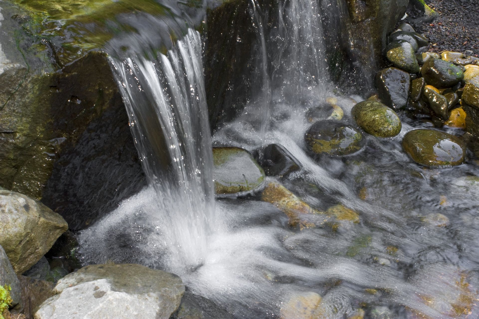 Small waterfall cascading over rocks into a stream, with mossy stones and clear water.