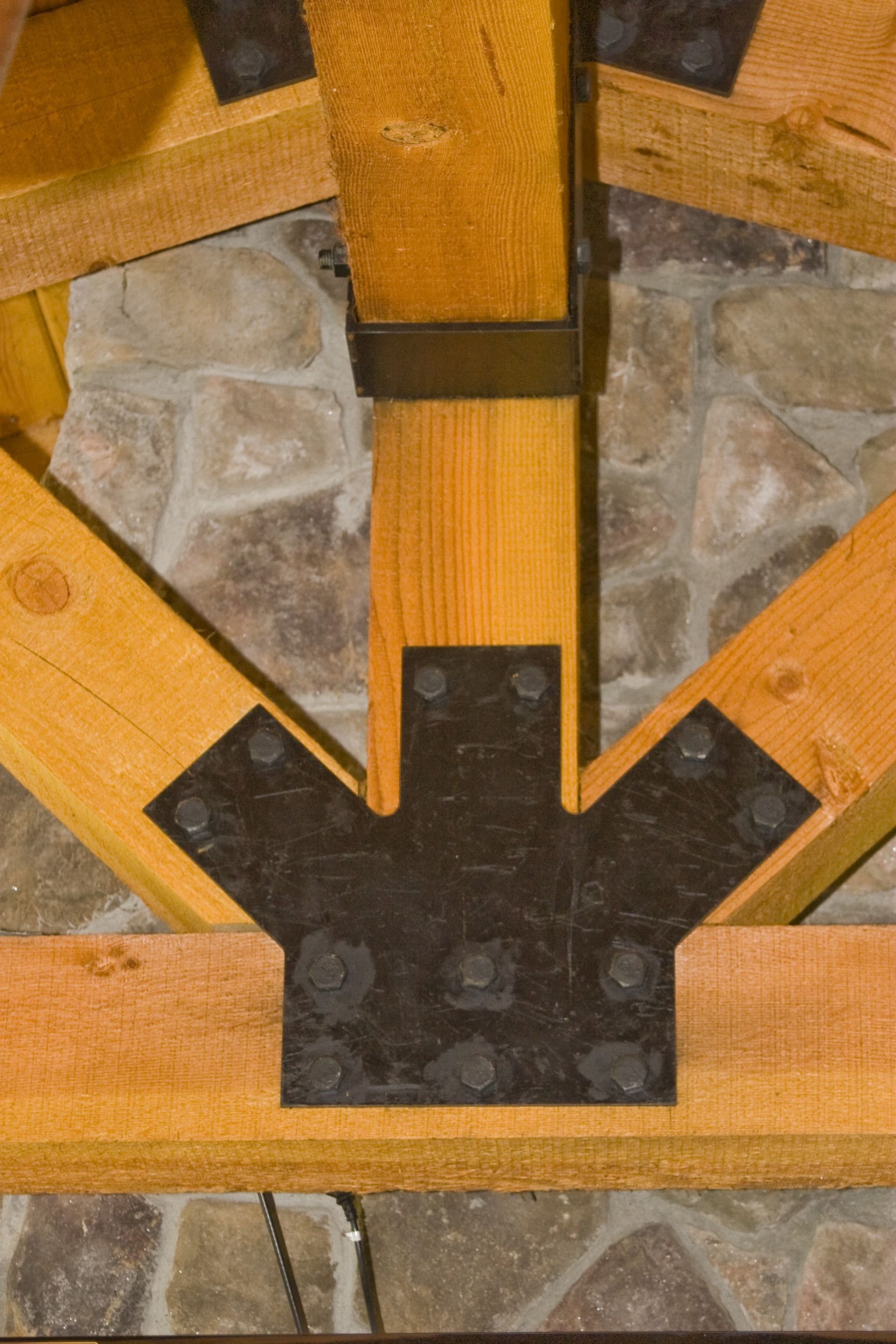 Close-up of a wooden structure with black metal brackets over a stone base.
