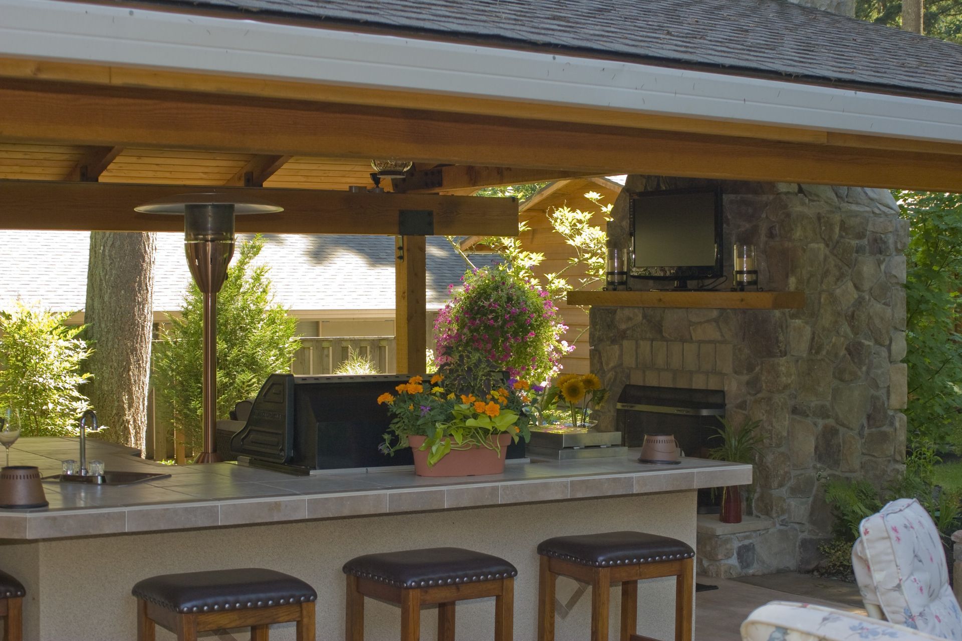 Outdoor stone bar with stools, hanging flower basket, and fireplace under a covered patio
