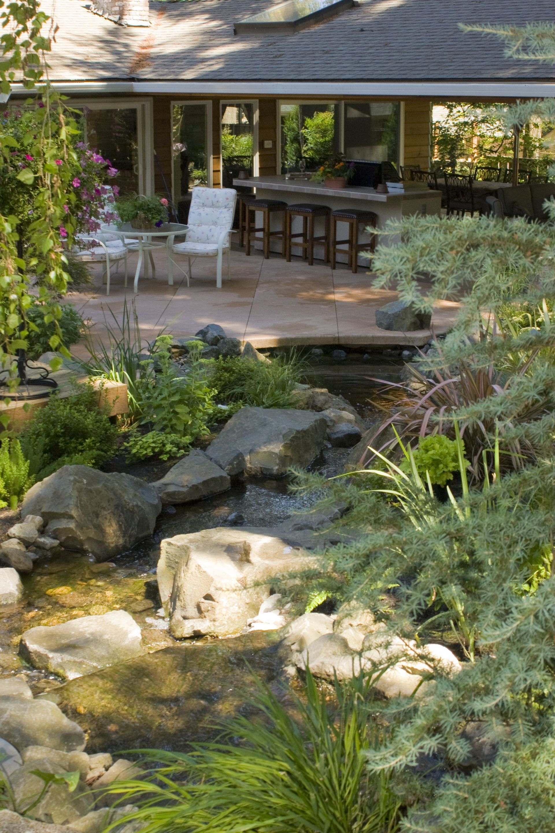 Backyard patio with bar seating beside a rock-lined pond and lush greenery