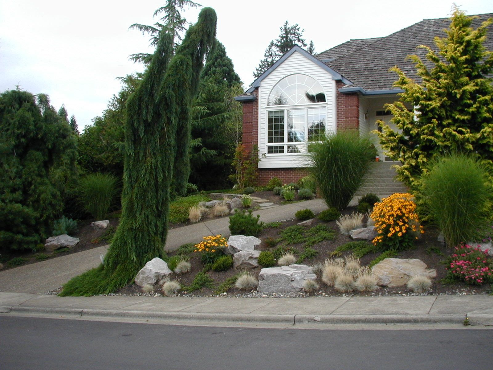 Landscaped front yard with shrubs, rocks, and a white brick house with arched window