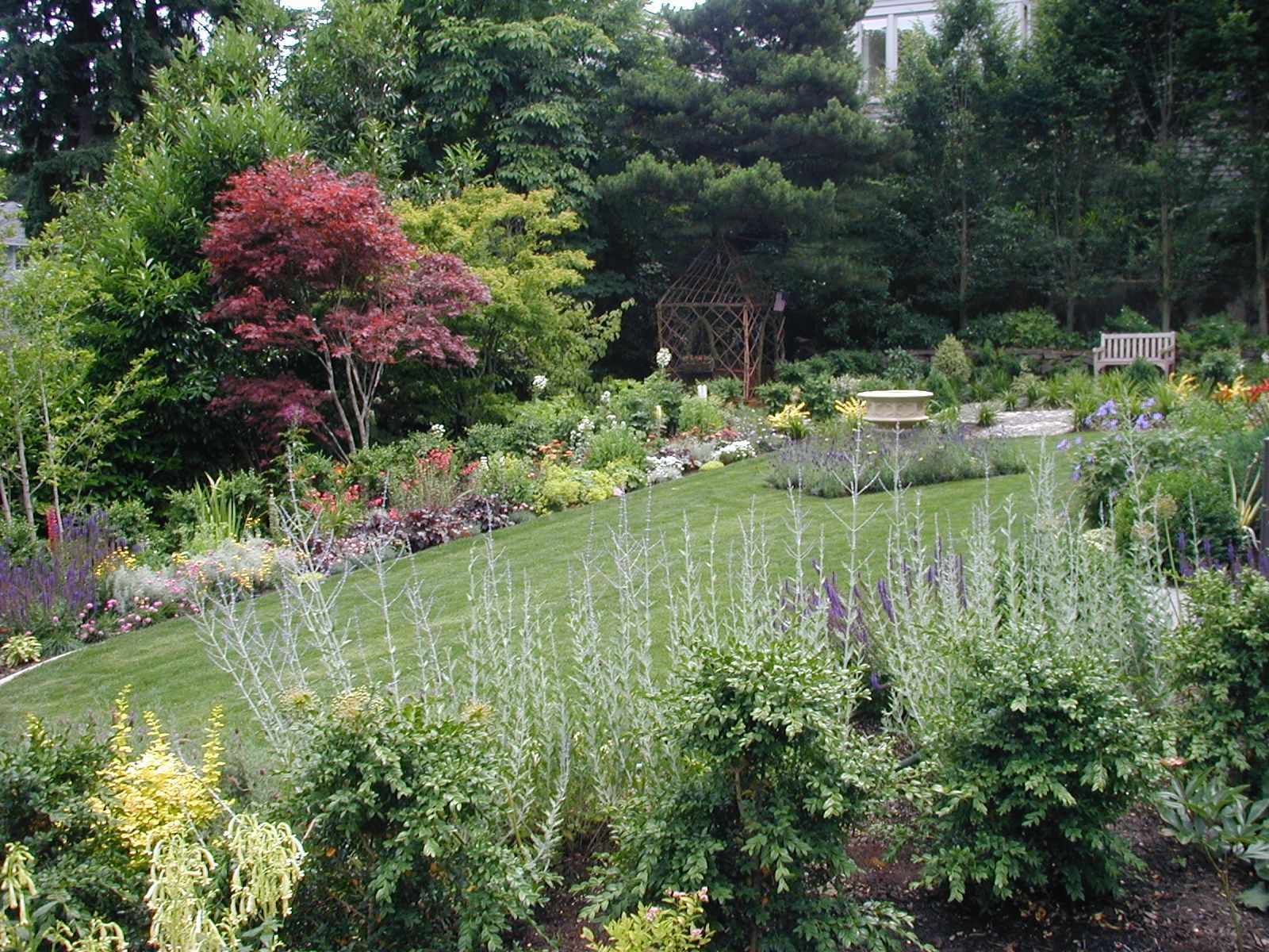 Lush garden with a small pond, blooming flowers, and trees in green and pink hues