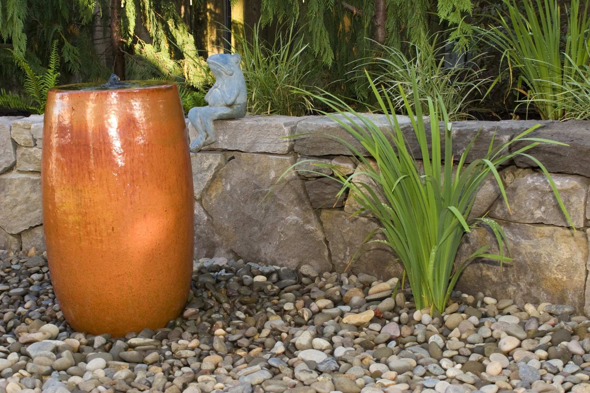 Orange ceramic vase in a rock garden beside a stone wall and green plants