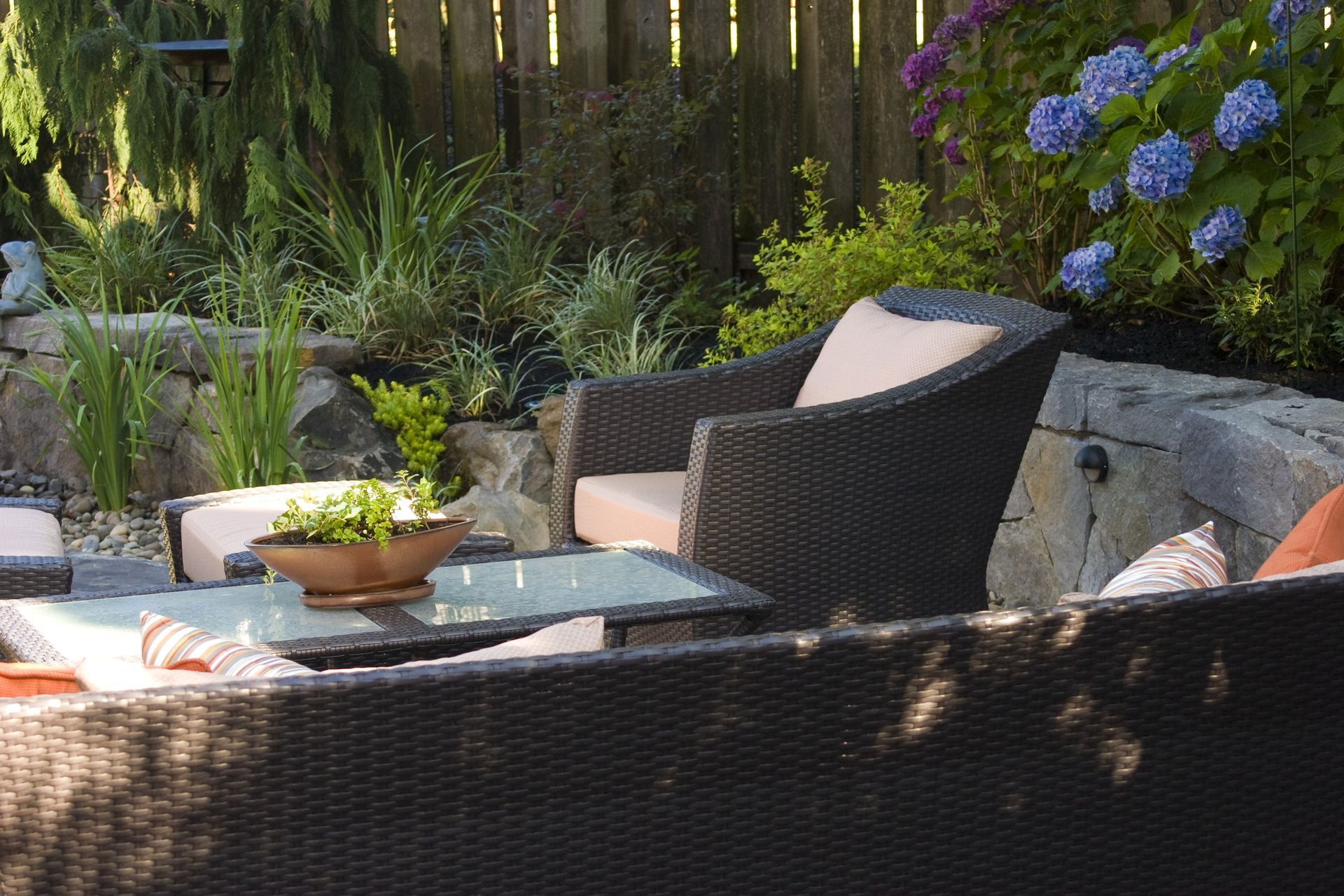 Outdoor patio with wicker chairs, glass table, and potted plants in a sunny garden