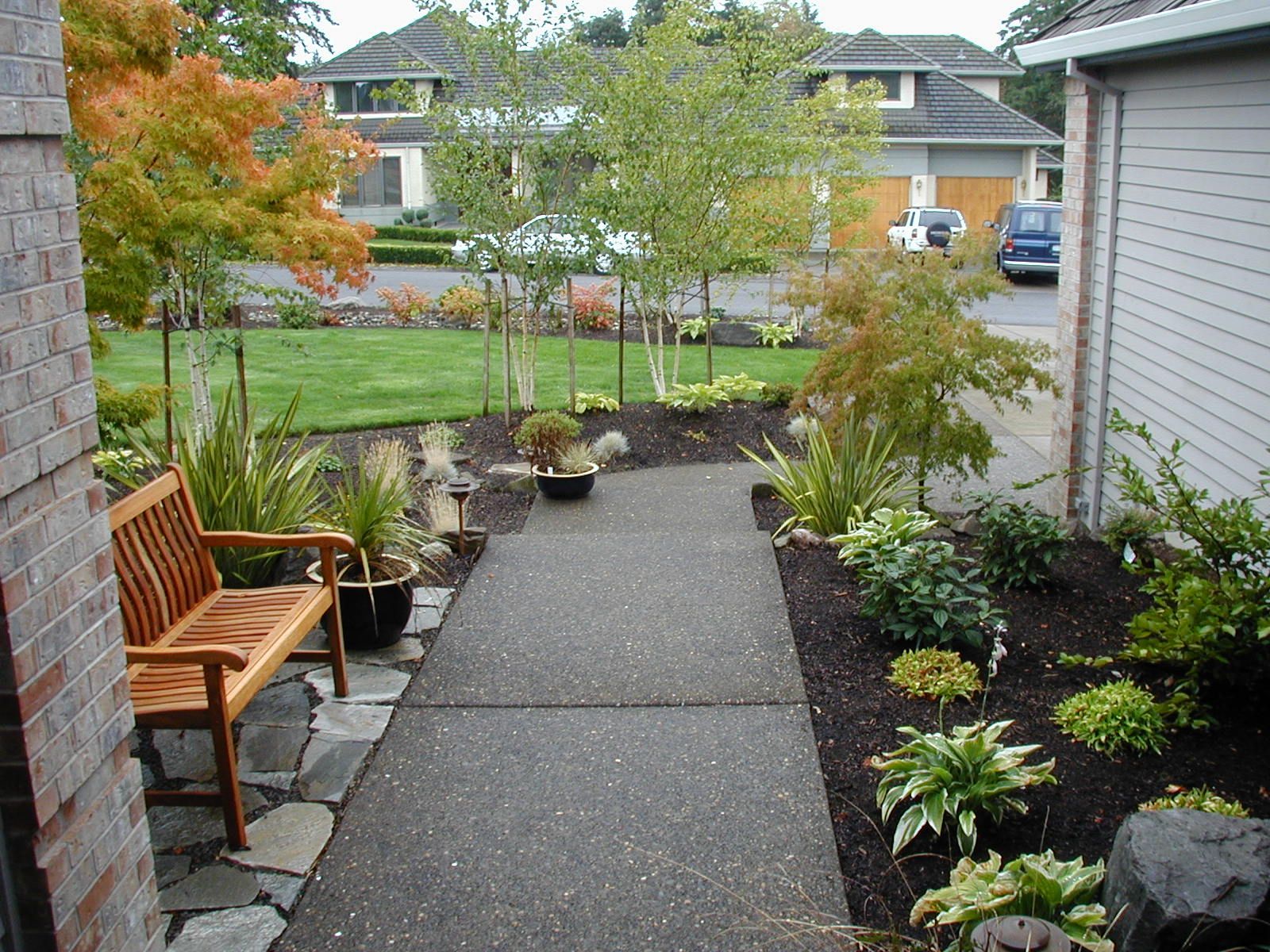 Front garden path with wooden bench, shrubs, and a view of houses across the lawn