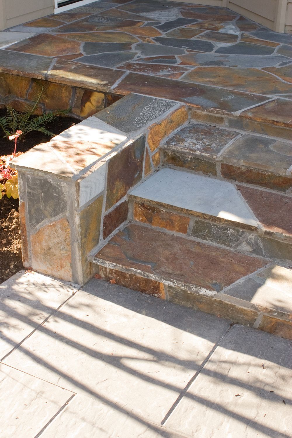 Stone walkway with small steps and a short wall, lit by sunlight and shadows.